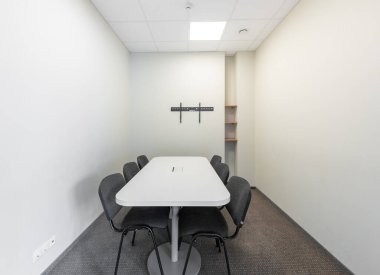 Beyaz bir masa, sandalyeler, boş duvarlar ve temiz ve minimalist iç tasarımı ön plana çıkaran geniş bir ışık içeren küçük bir konferans odası. Minimalist Tasarımda Modern Masa ve Sandalyeler.