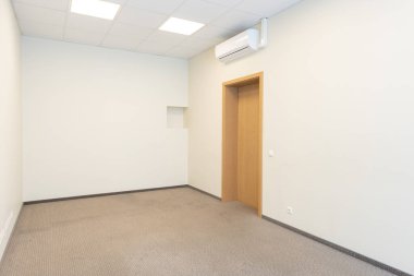 İçinde bej duvarlar, klima, halı döşeme ve ahşap bir kapı olan boş bir iç oda. Bej duvarları ve ahşap kapısı olan boş bir odanın minimalist iç mekanı..