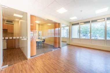 Geniş ve parlak bir ofis, cam duvarlar, ahşap döşemeler ve büyük pencerelerden süzülen doğal güneş ışığı. Cam bölümleri ve modern ahşap döşemeleri olan Parlak Ofis Alanı.