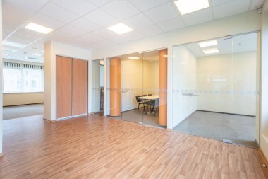 Geniş ve parlak bir ofis, cam duvarlar, ahşap döşemeler ve büyük pencerelerden süzülen doğal güneş ışığı. Cam bölümleri ve modern ahşap döşemeleri olan Parlak Ofis Alanı.