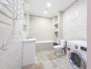 Parlak ve modern banyo, çamaşır makinesi, küvet, lavabo, bej kaplama duvarlar. Mükemmel organize ve donanımlı. Yıkama Makineli Modern Banyo, Küvet, Lavabo ve Bej Döşemeli Duvarlar.