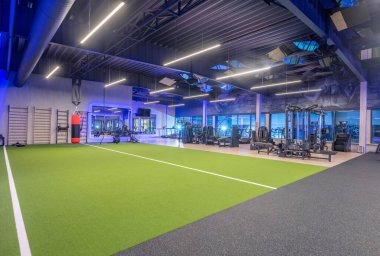 Çeşitli fitness ekipmanları, işlevsel çalışma alanları ve dinamik egzersizler ve kişisel eğitim faaliyetleri için canlı yapay çimen döşemeleri içeren geniş kapsamlı modern spor salonu..