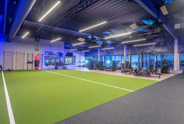 Çeşitli fitness ekipmanları, işlevsel çalışma alanları ve dinamik egzersizler ve kişisel eğitim faaliyetleri için canlı yapay çimen döşemeleri içeren geniş kapsamlı modern spor salonu..