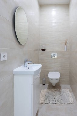 Çağdaş küçük bir banyo gösterişli bir tasarıma sahiptir. Bej duvar kiremitleri, lavabosu olan beyaz bir kiremit, duvara monte edilmiş bir tuvalet temiz bir boşluk yaratır. Ev İçi