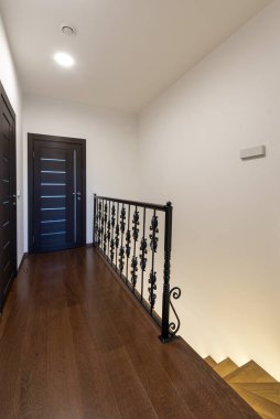 Karanlık ahşap döşemeleri ve şık bir siyah metal tırabzanı olan bir koridor gösteren çağdaş bir iç çekim. Minimalist tasarım basit ve zarif kapılara sahiptir. Ev İçi