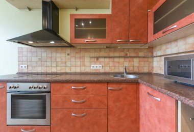 İçinde portakal kabini, granit tezgah, dahili fırın ve mikrodalga fırın bulunan çağdaş bir mutfak. Arka fıskiyeler açık bej ve kahverengi desenli..