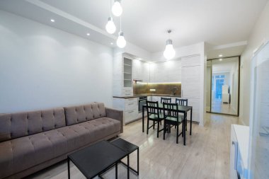 Rahat bir oturma alanı ve fonksiyonel bir mutfağı birleştiren geniş, çağdaş bir yaşam alanı. Tarafsız renklerle şekillendirilmiş, modern ışıklandırma. Modern Minimalist Ev Oturma Odası ve Mutfak İçi