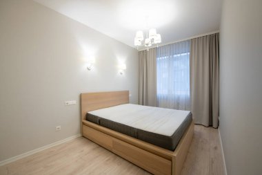 Parlak ve temiz bir yatak odası, ahşap mobilyalar, modern ışıklandırma, büyük pencereler, doğal gün ışığı. Ev Minimalist Yatak Odası İçi. Arka planda Büyük Boyut Yatak, Pencereler ve Perdeler.