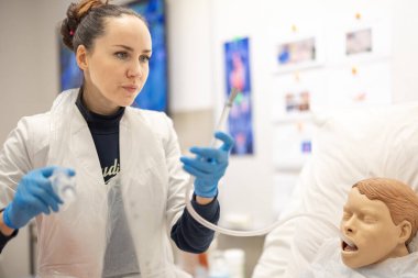 Bir hemşire, profesyonel eğitim ortamında gerçekçi bir hasta mankeni üzerinde tıbbi prosedürler uygular ve gerçek sağlık hizmetleri senaryolarını canlandırmak için tıbbi ekipmanlarla hassasiyet gösterir.