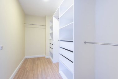 Beyaz açık raflar, askılı çubuklar ve ahşap döşemeler olan parlak bir dolap. Organize düzen giysi ve aksesuarlar için zarif ve işlevsel bir alan oluşturur. Modern Ev İçi