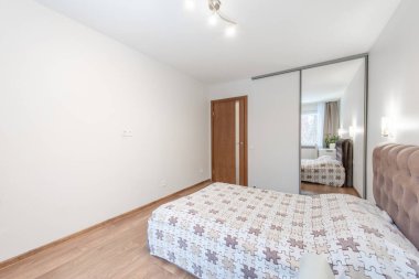 Rahat ve modern bir yatak odası. Şık bir yatak odası, ahşap döşeme ve minimalist dekor tarzı. Oda bir masa, bitkiler ve aynalı bir gardırop ile donatılmış..