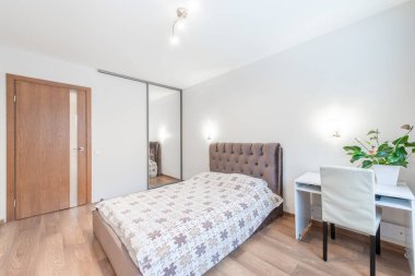 Rahat ve modern bir yatak odası. Şık bir yatak odası, ahşap döşeme ve minimalist dekor tarzı. Oda bir masa, bitkiler ve aynalı bir gardırop ile donatılmış..