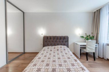 Rahat ve modern bir yatak odası. Şık bir yatak odası, ahşap döşeme ve minimalist dekor tarzı. Oda bir masa, bitkiler ve aynalı bir gardırop ile donatılmış..