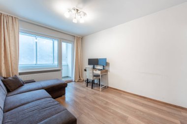 Parlak ve çağdaş oturma odasında rahat bir kanepe, parlak ahşap döşeme ve çift monitörlü işlevsel bir ofis masası sergileniyor. Modern Ev Oturma Odası İç Kanepe ve Ahşap Döşeme