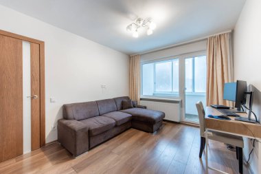 Parlak ve çağdaş oturma odasında rahat bir kanepe, parlak ahşap döşeme ve çift monitörlü işlevsel bir ofis masası sergileniyor. Modern Ev Oturma Odası İç Kanepe ve Ahşap Döşeme