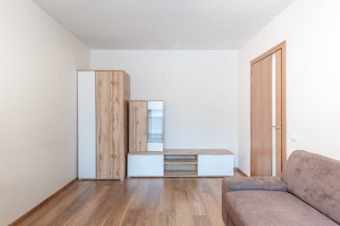 Büyük gri bir kanepe, ahşap döşeme ve minimalist mobilyaların bulunduğu rahat ve modern bir oturma odası. Nötr palet dinlenmek ve rahatlamak için hoş ve huzurlu bir atmosfer yaratır..