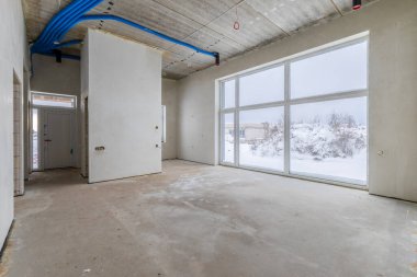 Odanın inşaatı devam ediyor. Duvarları alçılı, zemini beton. İnşaat halindeki bir evin beton tavanındaki havalandırma borularının kabloları. Geniş Açı