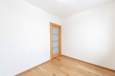 Parlak ve ferah boş bir odada ahşap bir zemin ve kapalı ahşap bir kapı var. Sakin ve basit iç tasarım rahatlatıcı bir ortam sağlar ve kişiselleştirme ve dekorasyon için mükemmeldir..