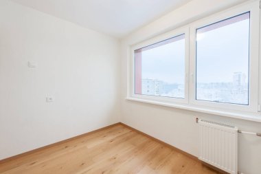 Ahşap döşeme, şehir manzarasını gösteren geniş bir pencere ve tarafsız duvarların yer aldığı güneşli boş bir oda. Gayrimenkul ve iç tasarım için mükemmel modern minimalist alanlar..
