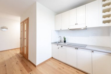 Beyaz dolap, geniş bir tezgah, ahşap döşeme ve bol miktarda doğal ışık sunan geniş bir pencere içeren parlak ve modern mutfak..