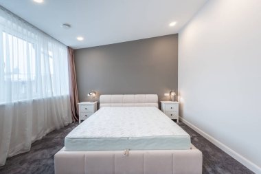 Lüks Ev Yatak Odası İçi. Büyük boy yatak, beyaz duvarlar ve tavan. Pencereler ve Perde. Kahve masası, yerde halı. LED Işık. Geniş Açı