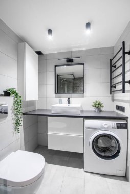 Beyaz Lavabolu Parlak Modern Lüks Ev Banyosu İç Tasarımı. Gri Duvarlar, Ayna ve Musluk döşemeleri. LED ışıkları. Duş Alanı, Isıtıcı, Çamaşır Makinesi. Geniş Açı