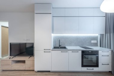 Klasik Parlak Ev Oturma Odası ve Mutfak İçi. Fırın, lavabo, dolaplar. Televizyon ekranı. İskandinav Tasarımı. Led Lights, Hardwood Zemini. Beyaz Duvarlar. Geniş Açı