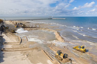 Plaj restorasyonu ve buldozerler. Denizin götürdüğü sahilin yeniden inşası için kazıcıyla birlikte borudan çamur akıyor. Plaj besinleri için çalışmalar devam ediyor. Drone Hava Çekimi