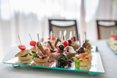 Şık bir ortamda cam tepside sunulan çeşitli aperatiflerin yakın çekimi yemek sanatını ve rafine yemek konseptini vurguluyor..