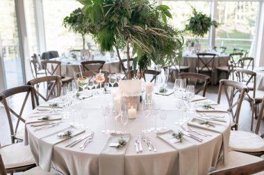 Çok güzel dekore edilmiş düğün masası zarif sofra takımı, mum ışığı atmosferi ve çarpıcı bir yeşillik süsü, sofistike bir atmosfer ve kutlama havası yayıyor.