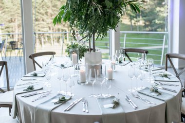 Çok güzel dekore edilmiş düğün masası zarif sofra takımı, mum ışığı atmosferi ve çarpıcı bir yeşillik süsü, sofistike bir atmosfer ve kutlama havası yayıyor.