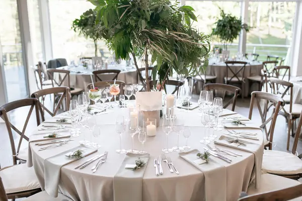 Çok güzel dekore edilmiş düğün masası zarif sofra takımı, mum ışığı atmosferi ve çarpıcı bir yeşillik süsü, sofistike bir atmosfer ve kutlama havası yayıyor.