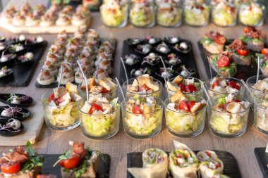 Çeşitli düğün aperatifleri, ambalajlar ve salatalar da dahil, tepsilerde yiyecek ve içecekler için güzel bir şekilde sergileniyor. Etkinlikler, partiler ya da kutlamalar için mükemmel, gurme yemek sunumu