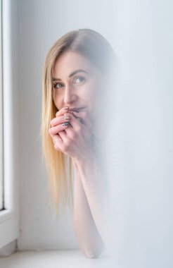 Düşünceli bir ifadeye sahip genç bir kadın pencereden bakar ve ortamı sakinleştirir..