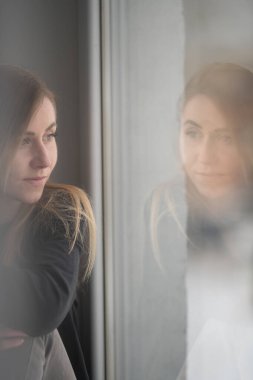 Yumuşak bir ışık pencerenin kenarındaki düşünceli bir kadını sarar, dinginliği ve iç huzuru çağrıştırır..