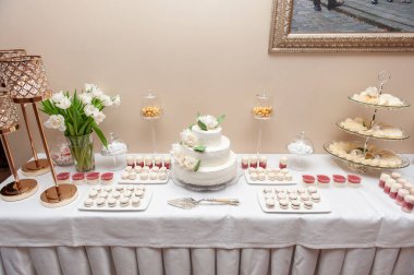 Katmanlı beyaz düğün pastası, badem kurabiyesi ve çiçeklerle süslenmiş güzel bir tatlı masası. Düğün ilhamları, güzel yemek etkinlikleri ya da tatlı sunumu örnekleri için ideal.