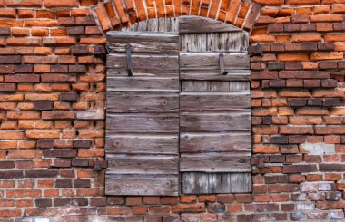 Kırsal ahşap panjurlar yıpranmış tuğla bir duvarda, tarihi mimari ve canlı dokular sergileniyor..