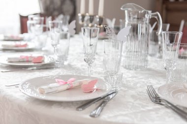 Özel bir toplantı için güzel bir yemek masası. Konuklara şenlikli ve davetkar bir ortam yaratmak için ince beyaz örtüler, kristal bardaklar ve pembe kelebek temalı dekorlar..