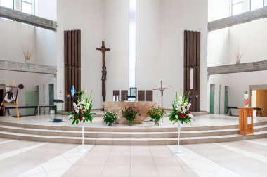 Çağdaş bir kilisenin içinde ahşap bir sunak haçı, çiçek aranjmanları ve ruhani toplanma ve tefekkür için ideal sakin bir ortam var..