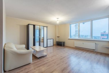 Modern mobilyaları, geniş pencereleri ve ahşap döşemeleri olan parlak ve ferah bir oturma odası. Bol miktarda doğal ışık ve sakin bir atmosfer sağlıyor.