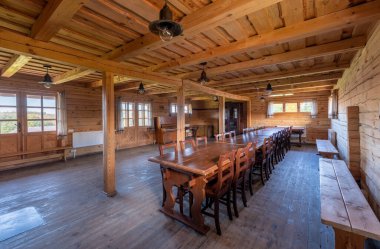 Uzun masalar, sandalyeler, konforlu bir şömine ve yan pencerelerden gelen doğal ışıklandırmanın yer aldığı taşralı ahşap yemek alanı, toplantılar veya halk yemekleri için sıcak ve davetkar bir ortam yaratıyor..