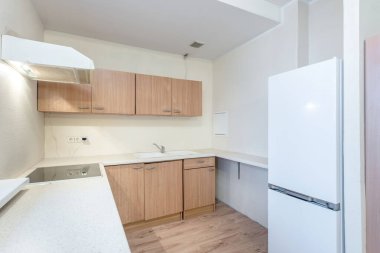 Parlak ve işlevsel mutfak, ahşap dolaplar, beyaz tezgahlar, ve modern bir buzdolabı, temiz ve minimalist bir stil yayıyor..