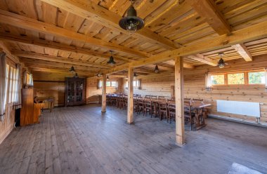 Uzun masalar, sandalyeler, konforlu bir şömine ve yan pencerelerden gelen doğal ışıklandırmanın yer aldığı taşralı ahşap yemek alanı, toplantılar veya halk yemekleri için sıcak ve davetkar bir ortam yaratıyor..