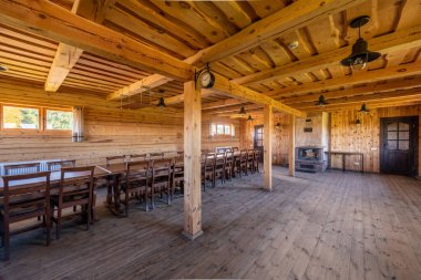 Uzun masalar, sandalyeler, konforlu bir şömine ve yan pencerelerden gelen doğal ışıklandırmanın yer aldığı taşralı ahşap yemek alanı, toplantılar veya halk yemekleri için sıcak ve davetkar bir ortam yaratıyor..