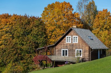 Uçsuz bucaksız ahşap bir ev. Geniş bir balkon. Renkli bir sonbahar ormanı düzenine yerleşmiş..