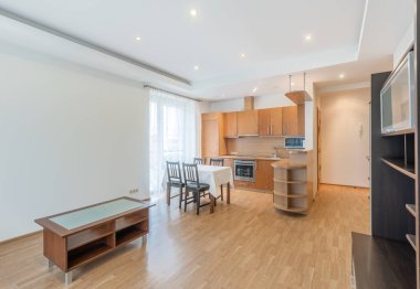 Modern mobilyaları, ahşap döşemeleri ve doğal gün ışığıyla aydınlatılan çağdaş tasarım unsurları olan birleşik oturma odası ve mutfağı olan parlak ve ferah bir daire.