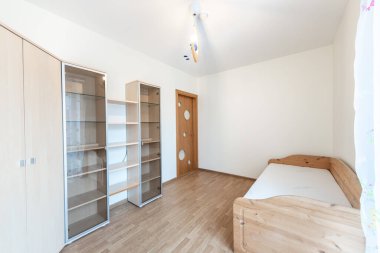 Basit ama işlevsel bir tasarım için tek bir ahşap yatak, cam ön raf ve ahşap mobilya içeren parlak ve minimalist bir oda..