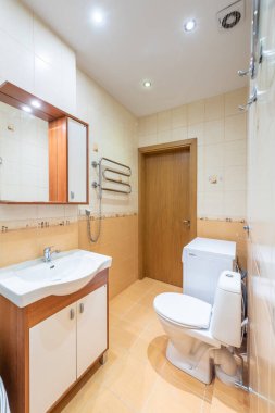 Döşeme duvarları, lavabosu, aynası, tuvaleti ve kompakt çamaşır makinesi olan parlak ve rahat bir banyo organize ve davetkar bir yer yaratıyor..