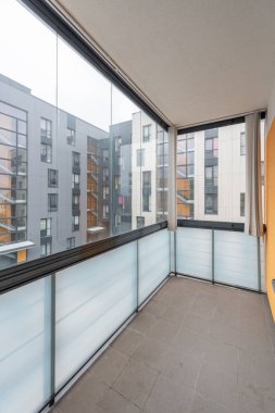 Camdan korkulukların ve kentsel konut binalarının manzaralı modern ev dairesi temiz minimalist estetiği vurguluyor.