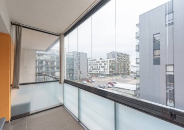 Camdan korkulukların ve kentsel konut binalarının manzaralı modern ev dairesi temiz minimalist estetiği vurguluyor.